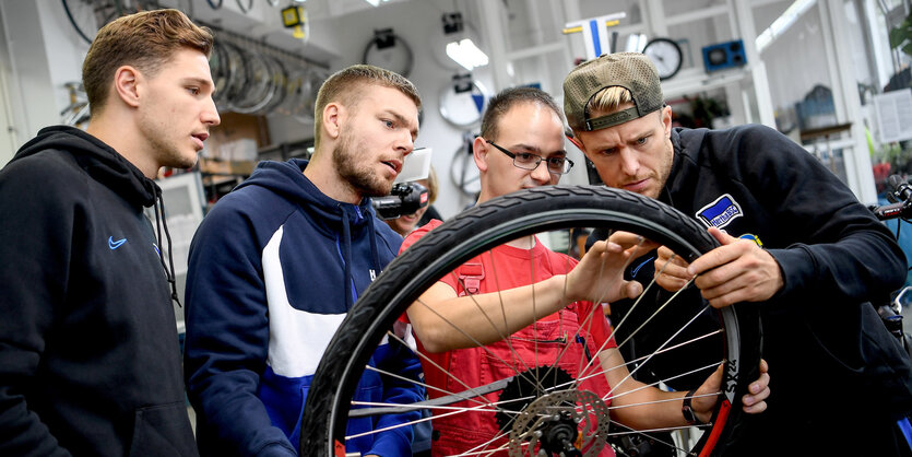 Drei Hertha-Spieler lassen sich erklären, wie man einen Fahrradschlauch wechselt