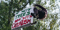 Besetzerin kletter an Seil entlang um ein Transpaerent aufzuhängen: up with trees down with captalism