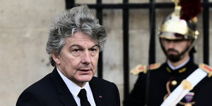 Mann mit vom Wind zerzaustem Haar läuft an eienm Uniformierten vorbei. Frankreichs neuer Vorschlag für die EU-Kommission: Ex-Wirtschaftsminister Thierry Breton