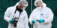 Zwei Männer in weißen Schtzanzugen betrachten einen Gegegstand in einem Plastikbeutel am Fundort von 39 Leichen in Essex.