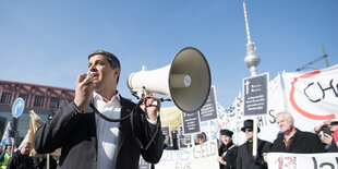 Raed Saleh hält ein Megaphon und redet zu Demonstrant:innen