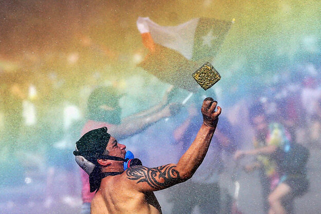 Ein chilenischer Demonstrant mit nacktem Oberkörper steht in einem Regenbogen und wirft etwas