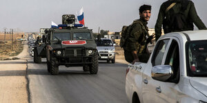Fahrzeuge der russischenMilitärpolizei auf einer Straße in Syrien. Im Vordergrund Kämpfer auf einem Pick-up