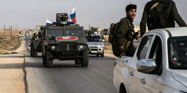Fahrzeuge der russischenMilitärpolizei auf einer Straße in Syrien. Im Vordergrund Kämpfer auf einem Pick-up
