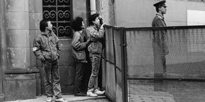 Dreiu Vietnamesen schauen an der innerdeutschen Grenze in Berlin über einen Zaun