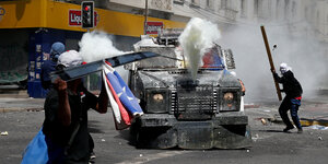 DemonstrantInnen schlagen in Valparaiso, Chile, mit Stangen auf ein gepanzertes Polizeifahrzeug ein