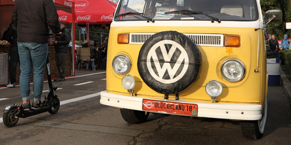 ein alter gelber VW-Bus, jemand fährt auf einem E-Roller daran vorbei