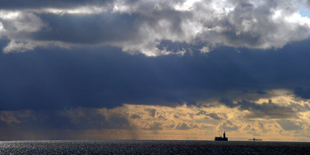 Schattenriss der Bohrinsel vor einem Horizont mit Abendrot und Wolken