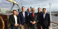 Sechs Bezirkspolitiker stehen auf dem Deck eines Schiffes im Hafen