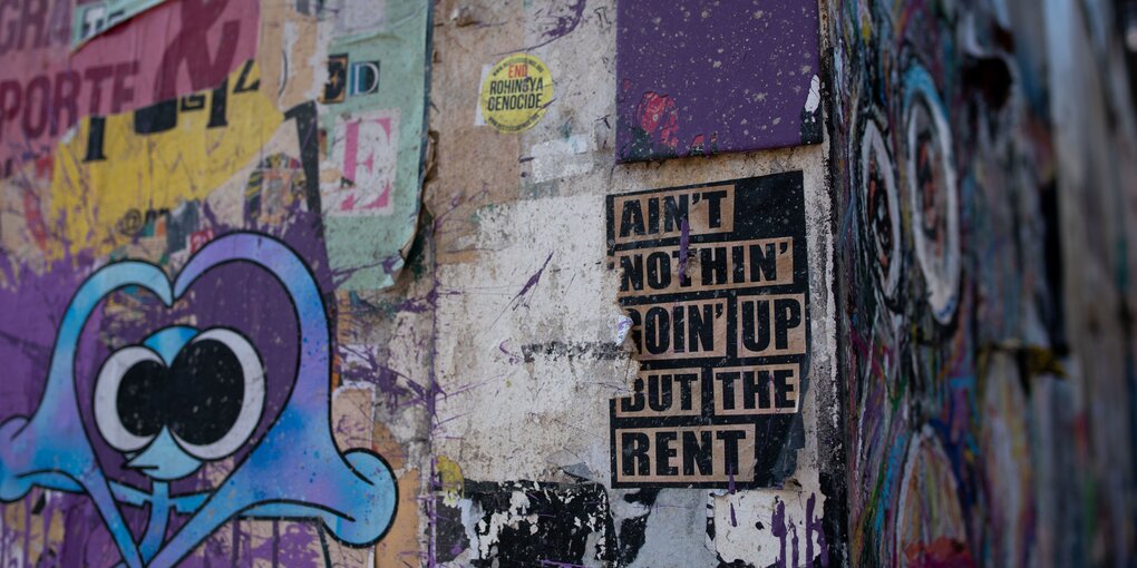 Eine bunt bemalte Hauswand auf der steht "ain't nothing going up but the rent"