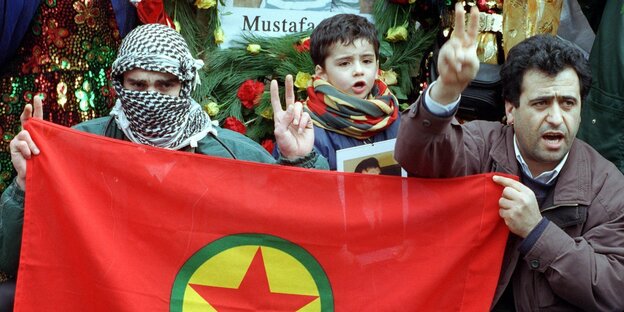 Demonstranten halten eine PKK-Fahne: roter Stern auf gelbem Untergrund in einem grünen Kreis; Flaggenhintergrund rot