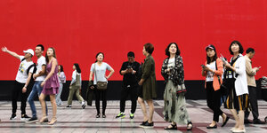 Menschen in China auf einer Straße vor einer roten Wand.