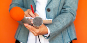 Eine Person hält zwei Mikrofone und einen Block in ihren Händen.