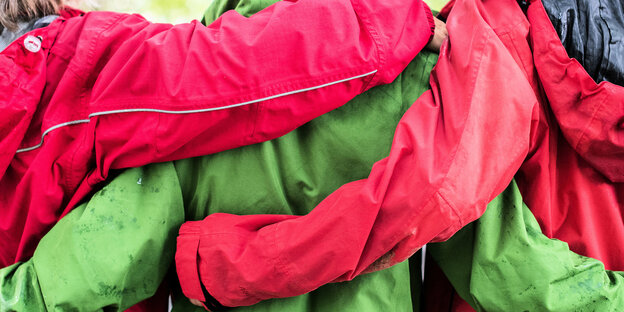 Drei Frauen tragen Regenjacken in roter und grüner Farbe