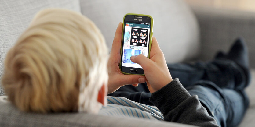 Junge liegt auf dem Sofa und schaut auf sein Smartphone