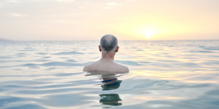 Ein Mann beim Baden, dahinter der Sonnenuntergang