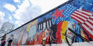 Menschen gehen auf einer Seite der Berliner Mauer der East Side Gallery entlang