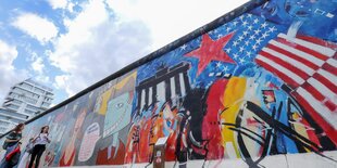 Menschen gehen auf einer Seite der Berliner Mauer der East Side Gallery entlang