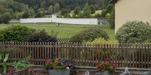 Ein Haus, dahinter eine Wiese auf der eine Mauer steht