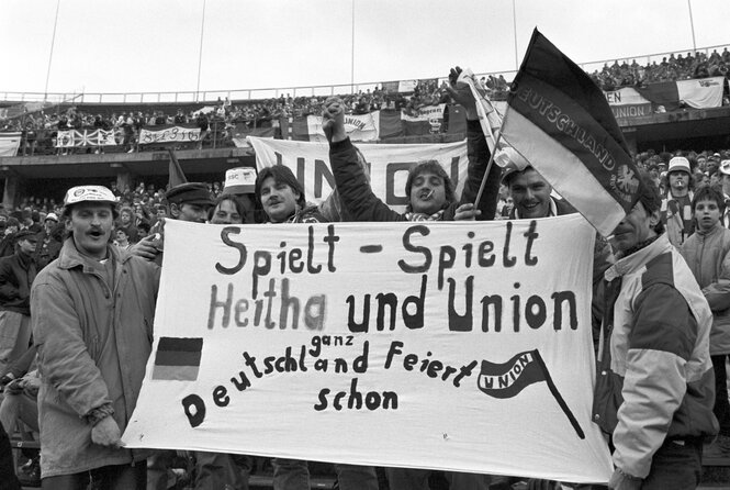 Hertha- und Union-Fans halten 1990 ein freundschaftliches Plakat hoch: Spielt spielt Hertha und Union, ganz Deutschland feiert schon