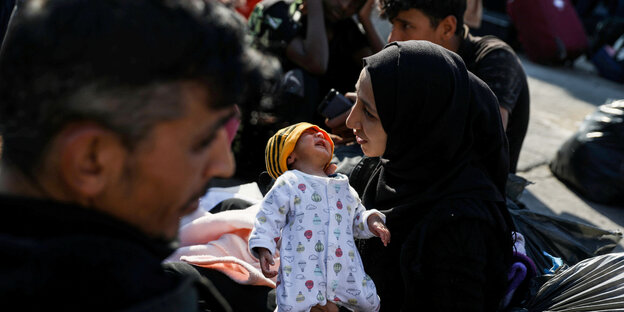 Eine junge Frau mit schwarzem Kopftuch hält ein Baby im Arm.