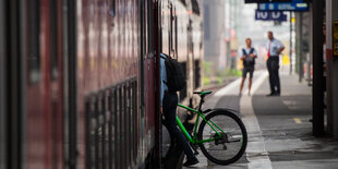 Ein Mann steigt mit seinem Fahrrad im Bahnhof in den Zug.