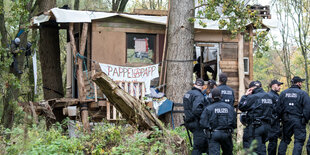 Eine Gruppe Polizisten steht vor dem Baumhaus mit einem Schild "Pappelapapp"