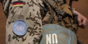 ein Soldat in Tarnuniform, auf seinem Arm sind eine Deutschlandfahne und ein UN-Logo
