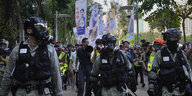 Polizisten mit Schutzkleidung und -masken begleiten eine Demonstration.