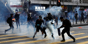 Demonstranten mit Helmen und Gesichtsschutz auf der Straße im Nebel aus Tränengas.