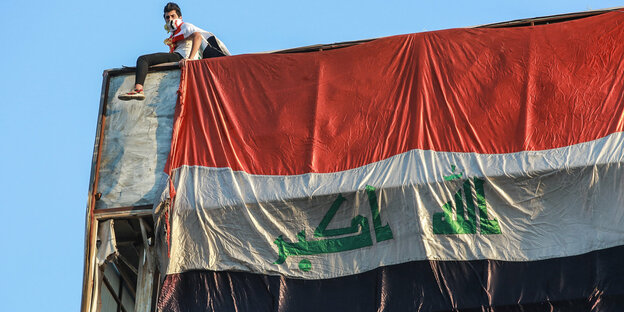 Ein Demonstrant sitzt auf einem Gerüst, über das eine große irakische Flagge gespannt ist