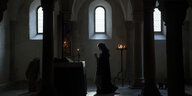 Eine Frau im Mantel betet in einer dunklen Kirche.