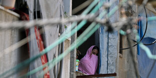 Eine Frau in einem rosa Tuch guckt aus einem Fenster in Gaza, davor hängen grüne Kabelleitungen