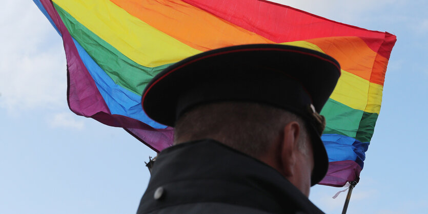 Polizist von hinten fotografiert vor einer wehenden Regenbogenfahne.