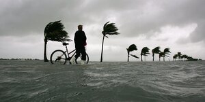 Mann mit Fahrrad auf einem überfluteten Küstenboulevard in Florida