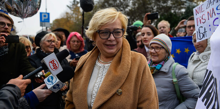 Eine Frau im Mantel umringt von Journalisten