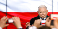 Kaczyński sitzt auf einer Rednertribühne, vor ihm halten Menschen Handys hoch