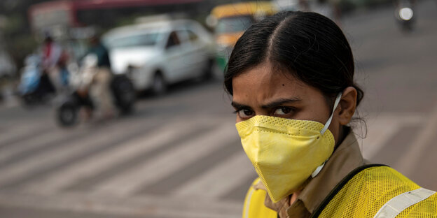 Eine junge Frau steht an einer Straße und trägt eine gelbe Atemmaske