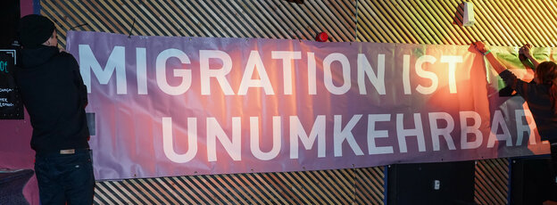 Zwei Menschen hängen ein Banner mit der Aufschrift "Migration ist unumkehrbar" auf.