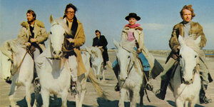 Vier schick gekleidete Männer und eine Frau reiten durch eine Wüste