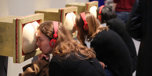 Ausstellungsbesucherinnen schauen in einen Guckkasten, der aussieht wie ein Hintern