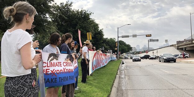Menschen stehen am Straßenrand und protestieren gegen die Klimapolitik von Exxonmobil