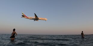 Badende Touristen schauen einem Flugzeug zu, das über das Meer fliegt