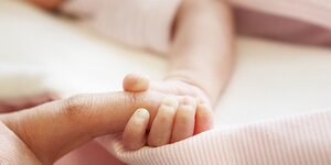 Das Händchen eines neugeborenenKindes hält den Finger eines Erwachsenenfest