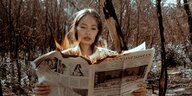 Ein junge Frau liest eine Zeitung, deren oberer Rand brennt