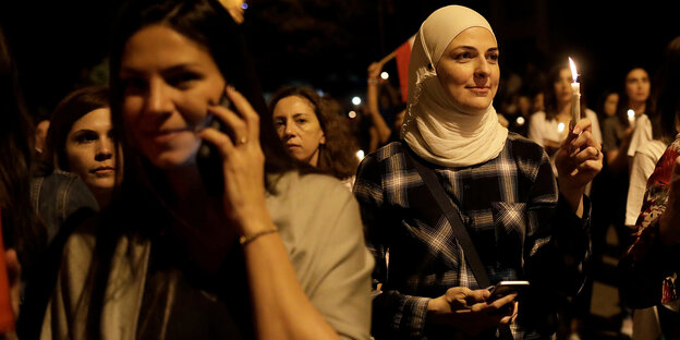 Demonstrantinnen halten Kerzen, eine telefoniert