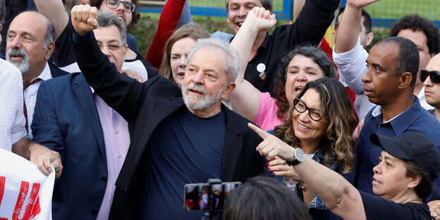 Brasiliens Ex-Präsident Lula steht inmitten von Menschen und streckt den Arm in die Luft.