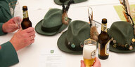 Auf einem Tisch liegen vier Hüte einer Schützenbruderschaft. Hände halten Bierflaschen.
