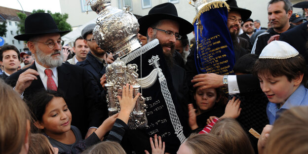 Zwei Rabbiner tragen Torarollen, begleitet von Kindern