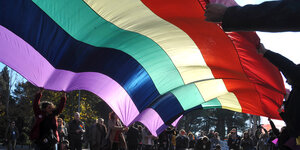 Männer und Frauen halten eine große Regenbogenfahne.
